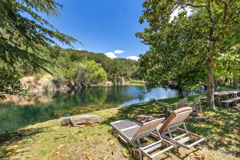Adirondack chairs and a teak lounger on the lawn beside the estate's spring-fed swimming pond, ringed by oak and bay woodland.